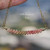 Minimalist curved floating shell necklace shown hanging naturally to highlight the soft curved design, handcrafted shell pattern, detailed workmanship, and how the necklace gently floats along the neckline. Genuine Kahelelani shells from Niʻihau in Keʻokeʻo, green, pink flower, and soft pink tones with gold filled chain.