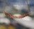 Hanging view of a minimalist Kahelelani shell necklace displaying a natural island blend of pink, green, burgundy, and dark brown shells arranged in a softly curved floating design that showcases the handcrafted pattern and delicate Hawaiian shell workmanship.