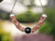 Full hanging view of the handcrafted triple strand poepoe necklace showing how the necklace naturally drapes while displaying the soft blend of pink, green, and keʻokeʻo Kahelelani shells with a baroque peacock Tahitian pearl focal point.