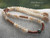 Outdoor display of a handmade 26-inch traditional Niʻihau shell lei with Kipona design, genuine Momi and Kahelelani shells, peacock Tahitian pearl, and natural Hawaiian craftsmanship.