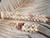 Handmade Niʻihau Kipona shell earrings displayed beside the matching Momi Pikake section of a traditional Niʻihau shell lei, showcasing coordinated craftsmanship.