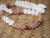 Angled view of a handmade Kipona Style Hawaiian shell necklace featuring colorful Kahelelani Poepoe sections, off-white Momi shells, and Granulated Cowrie shell clasp displayed on a woven lauhala mat.