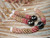 Handcrafted Triple Strand Poepoe Kahelelani shell necklace from Niʻihau held against a natural green background, showing colorful size 11 shells and a medium-dark baroque Tahitian pearl
