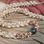 Close-up of Niʻihau shell lei #2025 showing white Puka shell flower design with pink and green Kahelelani shells surrounding a dark Edison pearl.