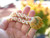 Hand-held Niʻihau shell necklace showing off-white Puka shells, soft pink and green Kahelelani and yellow green gray pink Sunrise shell
