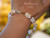 Close-up of Hawaiian shell bracelet worn on the wrist, showing the decorative 14K gold-filled clasp and intricate Niʻihau Momi and Kahelelani shellwork.