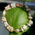 Full view of Hawaiian shell bracelet displayed on a green tropical leaf, featuring Niʻihau Momi and Kahelelani shells, Keshi pearls, Puka shells, and 14K gold-filled accents.