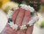 Hand-held Niʻihau Kipona shell bracelet showing its size and detailed Momi and Kahelelani shell arrangement, dark pearl centerpiece, and decorative gold-filled safety clasp.