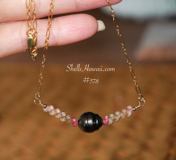A delicate Hawaiian shell necklace hanging to showcase the dark silver-black Tahitian pearl and colorful hot pink, green, and Keʻokeʻo Kahelelani shells. A rare Hawaiian shell necklace that embodies coastal aesthetic jewelry.