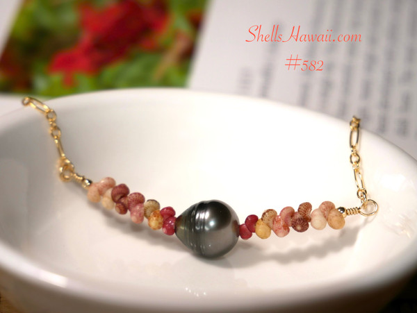 An elegant coastal Hawaiian shell necklace resting in a white dish, highlighting the natural color flow of red-hot pink, yellow Kamoa green, soft pink, brown, and off-white Kahelelani shells with a 9.5 mm Tahitian pearl.