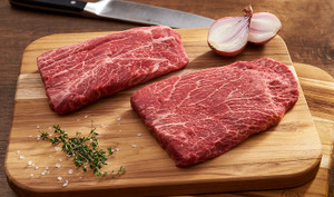 Pictured are 2 uncooked Linz Heritage Angus Petite Flat Iron Steaks with chopped onion and rosemary
