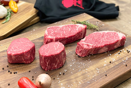 Pictured are 2 uncooked Linz Heritage Angus New York strip steaks and 2 uncooked Linz Heritage Angus tenderloin filets (filet mignons) on a cutting board.