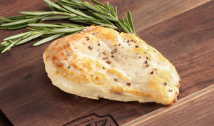 Pictured is a cooked chicken breast garnished with rosemary on a cutting board.