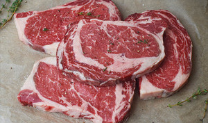 Pictured are 4 uncooked Linz Heritage Angus boneless ribeyes on a cutting board.