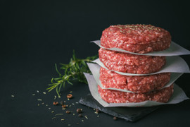 Pictured are uncooked Linz Angus PRIME Steak Burgers  on a cutting board with salt pepper and herb garnish