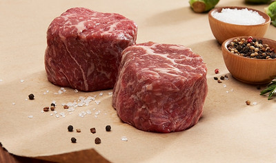 Pictured are 2 uncooked Linz Heritage Angus ribeye filets on a cutting board, cut to look like filet mignon but from the center of the ribeye