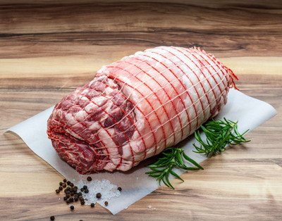 Pictured is an uncooked Leg of Lamb on a wood table with rosemary, salt and pepper garnish