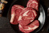 Pictured is 4 uncooked Linz Heritage Angus reserve boneless dry aged ribeyes in a frying pan