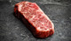 Pictured is 1 raw Westholme Wagyu Boneless Strip Steak 20 oz on a cutting board.