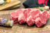 Pictured are 4 uncooked Linz Heritage Angus boneless ribeyes with a container of seasoning on a cutting board.