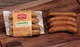 Pictured is a pack of Jalapeno Cheddar Bratwurst By Chef Martin sitting next to fully cooked jalapeno brats on a table.