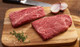 Pictured are 2 uncooked Linz Heritage Angus Reserve flat iron steaks on a cutting board