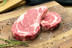 Pictured are 2 uncooked Linz Heritage Angus boneless USDA Prime steaks on a cutting board.