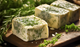 Pictured is Herb Mushroom Butter cut into cubes with whole herbs scattered on a cutting board.