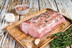 Pictured is an uncooked Iberico Pork Loin on wooden table with garlic and herb garnish