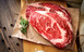 Pictured are two uncooked Boneless Ribeye Steak USDA Prime on cutting board with butcher paper and rosemary 