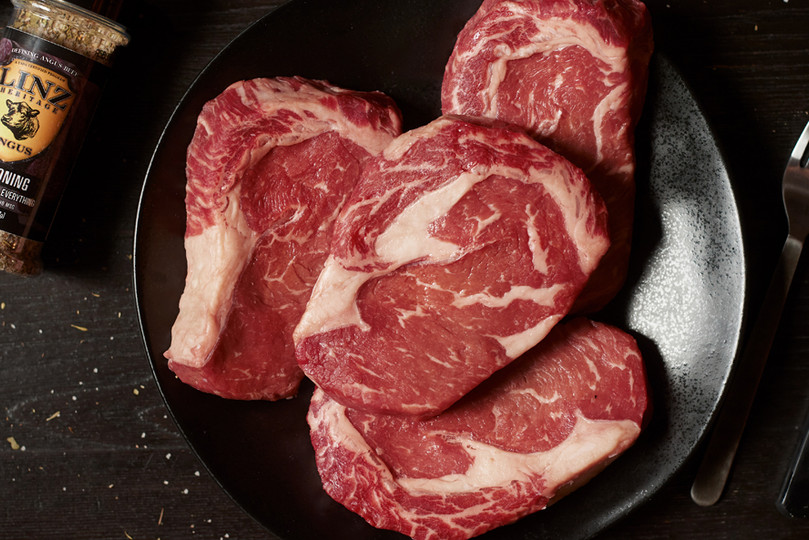 Pictured is 4 uncooked Linz Heritage Angus reserve boneless dry aged ribeyes in a frying pan