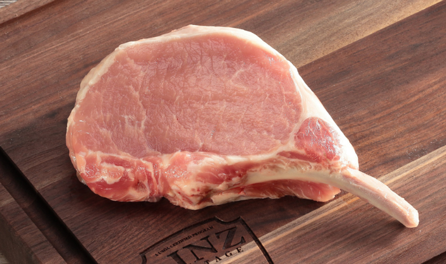 Pictured is an uncooked thick cut bone-in pork chop on a cutting board.