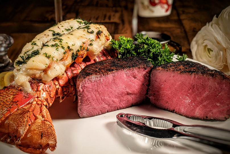 Pictured is a cooked Linz Heritage Angus filet mignon cut in half and a Maine lobster tail on a plate.