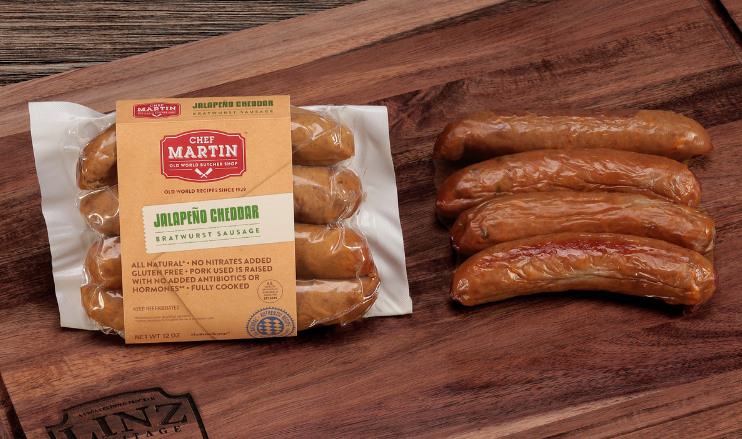 Pictured is a pack of Jalapeno Cheddar Bratwurst By Chef Martin sitting next to fully cooked jalapeno brats on a table.