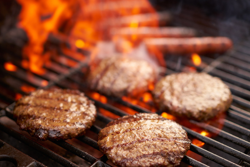 Pictured are four Linz Heritage Angus steak burgers cooking on an open grill.