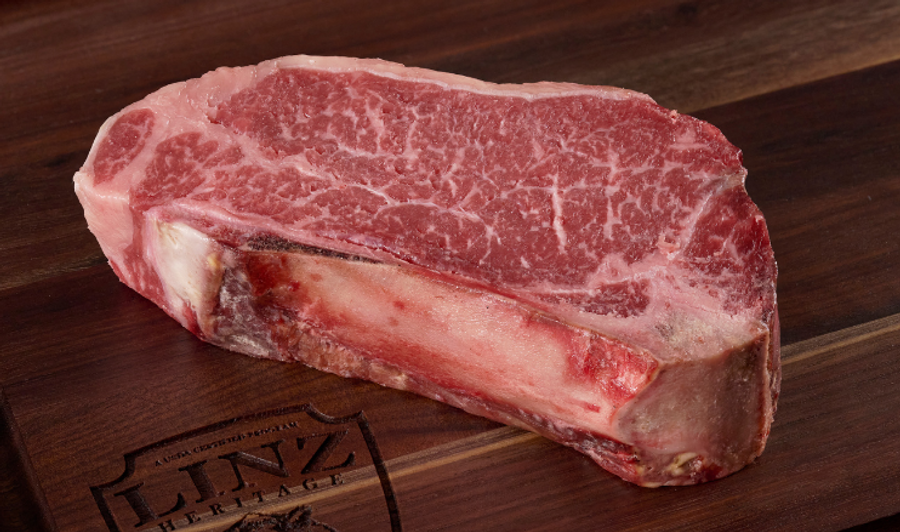 Pictured is an uncooked Bone-In Strip Steak USDA Prime Dry Aged on cutting board