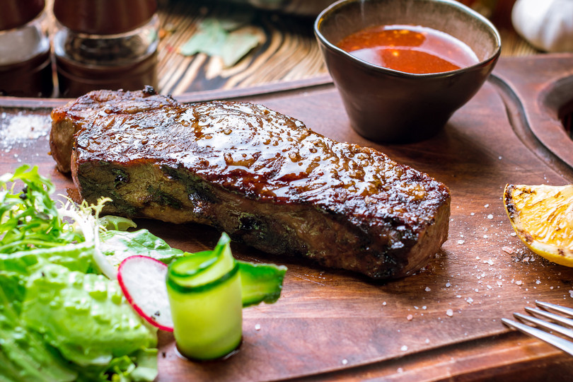 Pictured is a fully cooked Linz Heritage Angus Long Island Strip Steak on a cutting board.