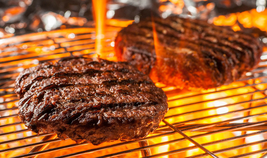 Pictured are 2 cooking Linz Heritage Angus steakhouse burgers on an open grill.