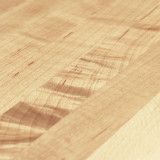 A focused view of the modern Parsons table surface, capturing the warm tones of the solid maple wood grain.