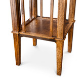 Close-up of the plant stand’s base showing the recessed wood shelf, vertical spindles, corner posts, horizontal rails, and four tapered legs.