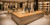 Luxury women’s fashion boutique with a large Quarter Sawn White Oak wide plank countertop, dressed mannequins, clothing racks, illuminated handbag displays, and warm modern lighting.