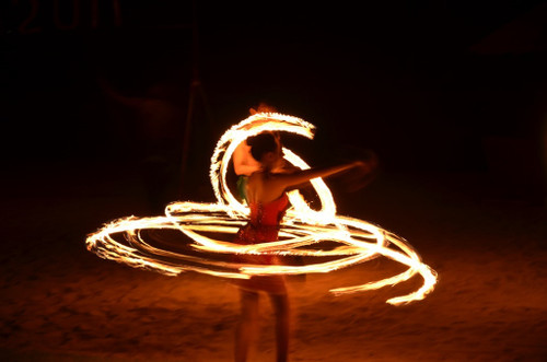 Female dancer in a red sequinned outfit with spinning fire lit torch