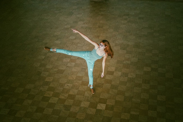 Female dancer with long red hair and glasses wearing teal top and pants 