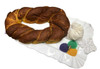 Creole Foods of Louisiana Traditional King Cake with icing on side, round twisted bread with golden-brown crust, served on a decorative white plate with purple, green, and orange colored sugar and a small gold cross charm.