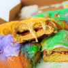 Gambino's Traditional King Cake with icing on side, showing a slice revealing the rich filling inside, surrounded by colorful icing and sprinkle decorations.