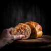 M&R Creole's Mini Stuffed Bread 12ct, close-up of a person holding a halved mini stuffed bread showing the savory meat filling inside.