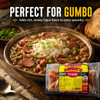 Savoies Pork Tasso 8oz, packaged smoked pork product, shown in front of a Cajun gumbo dish with rice and green onions, garnished with chopped green onions, with a loaf of bread in the background.