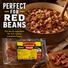 Savoies Pork Tasso 8oz, package of smoked pork tasso with yellow and red label, set on a wooden surface with cooked red bean and rice dish in a bowl, garnished with chopped green onions, highlighting Louisiana flavors.
