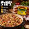 Savoies Andouille 16oz, packaged smoked Cajun sausage on a wooden surface with a pasta dish with sausage slices, red and green peppers, and creamy sauce in a skillet.