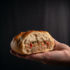 M&R Creole's Stuffed Bread 4ct, close-up of a person's hand holding a half of stuffed bread showing savory meat and vegetable filling inside.